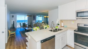 A modern kitchen with a dishwasher, oven, and microwave. There is a dining area with a table and chairs, and a view of the ocean through large windows. - Ilikai Marina One Bedroom Harbor View Condos - Walk to Ala Moana Beach Park! (Honolulu)