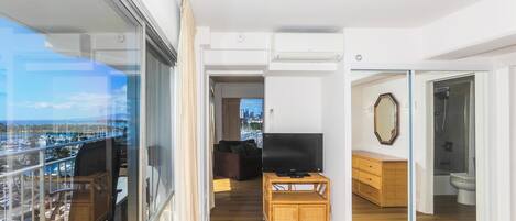Un apartamento moderno con balcón, una sala de estar con sofá y televisor, un mueble de madera y un baño con ducha e inodoro.