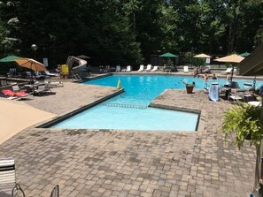 A swimming pool with lounge chairs and umbrellas, surrounded by trees.