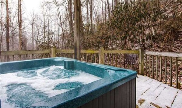A hot tub surrounded by a wooden deck and a wooden fence, with trees in the background.