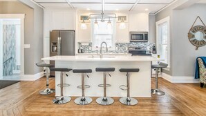 Une cuisine moderne dotée d’un îlot central, de tabourets de bar, d’appareils électroménagers en acier inoxydable et de luminaires suspendus.