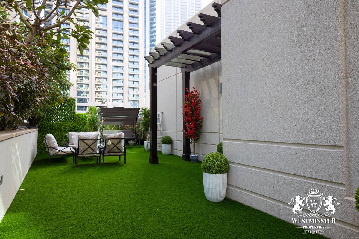 A courtyard with artificial grass, outdoor furniture, potted plants, and a pergola.