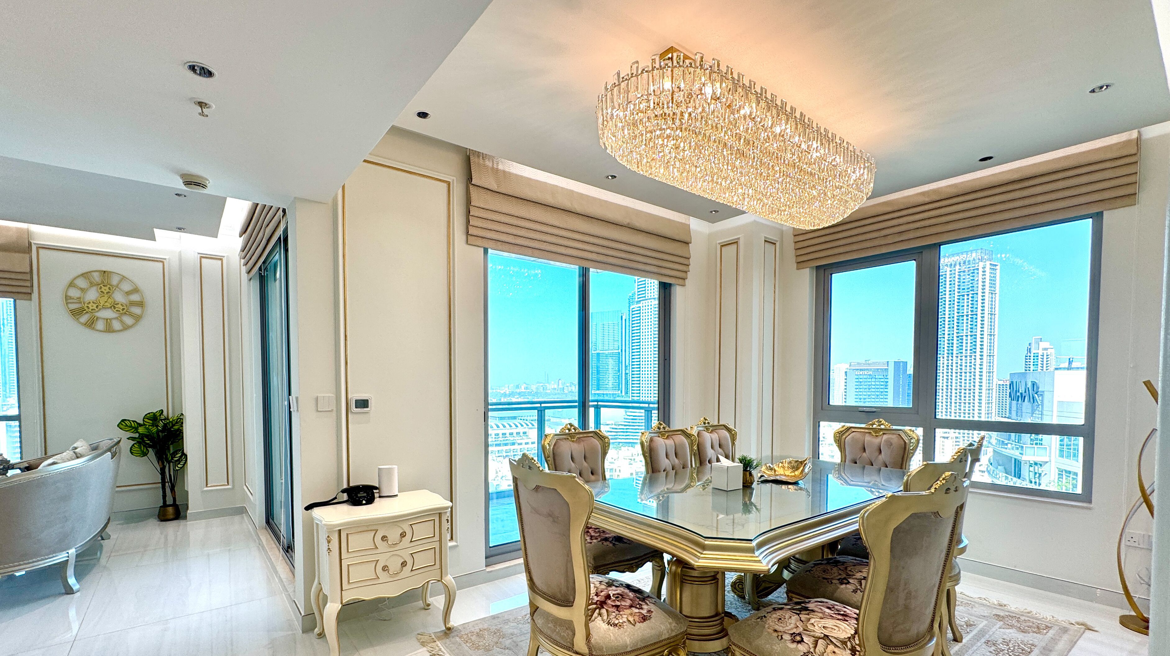 A spacious dining area with a large chandelier, elegant chairs, and a city view through large windows.