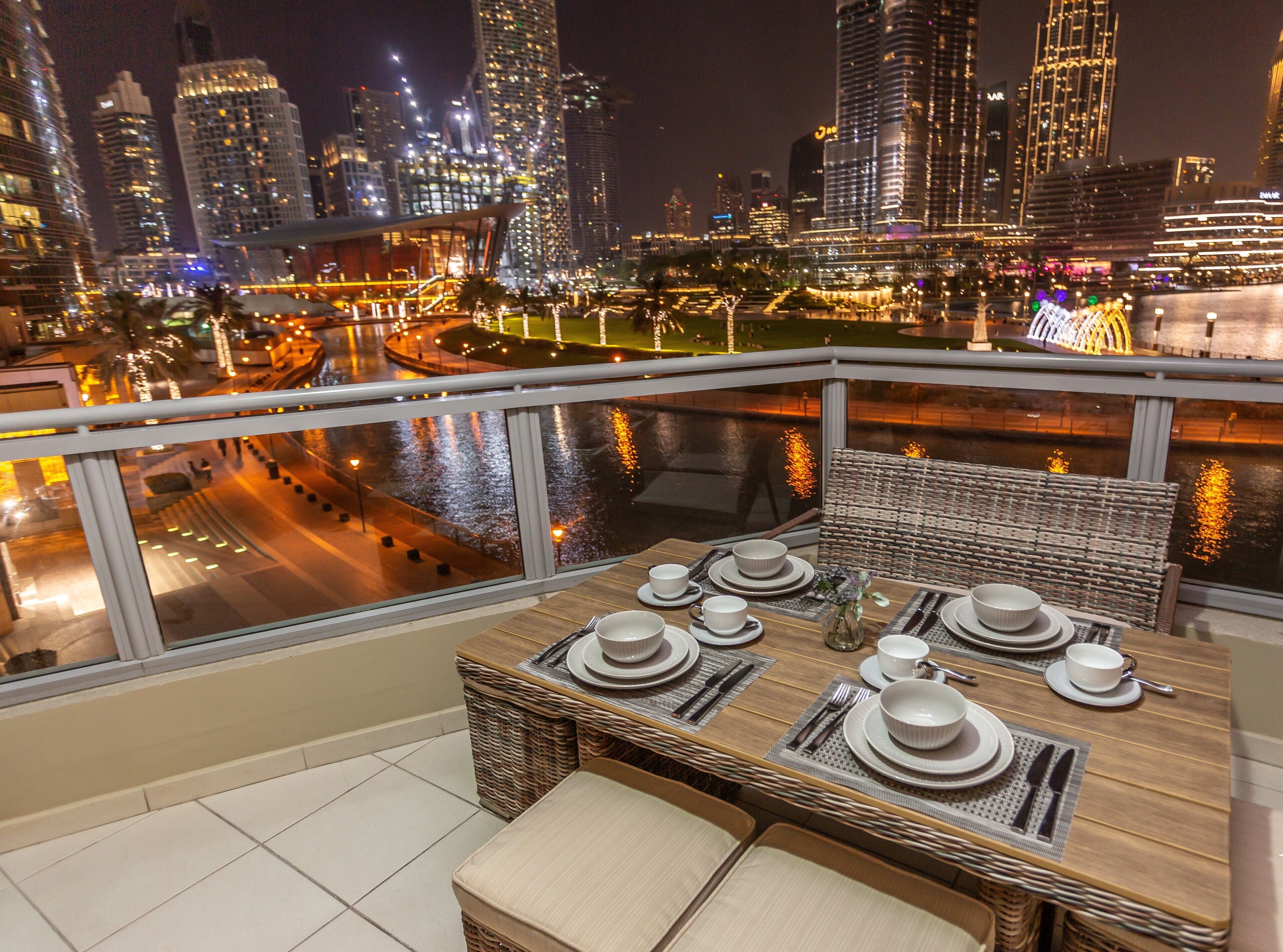 Comedor con una mesa dispuesta para cuatro, con vistas a un paisaje urbano con edificios iluminados y un río.