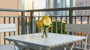 Un balcon avec une table et des chaises, un vase rempli de fleurs et une vue sur le paysage urbain.