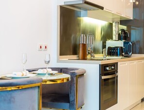 Eine moderne Küche mit Edelstahlgeräten, einem Backofen und einer Kaffeemaschine. Es gibt einen Essbereich mit einem runden Tisch und Stühlen.