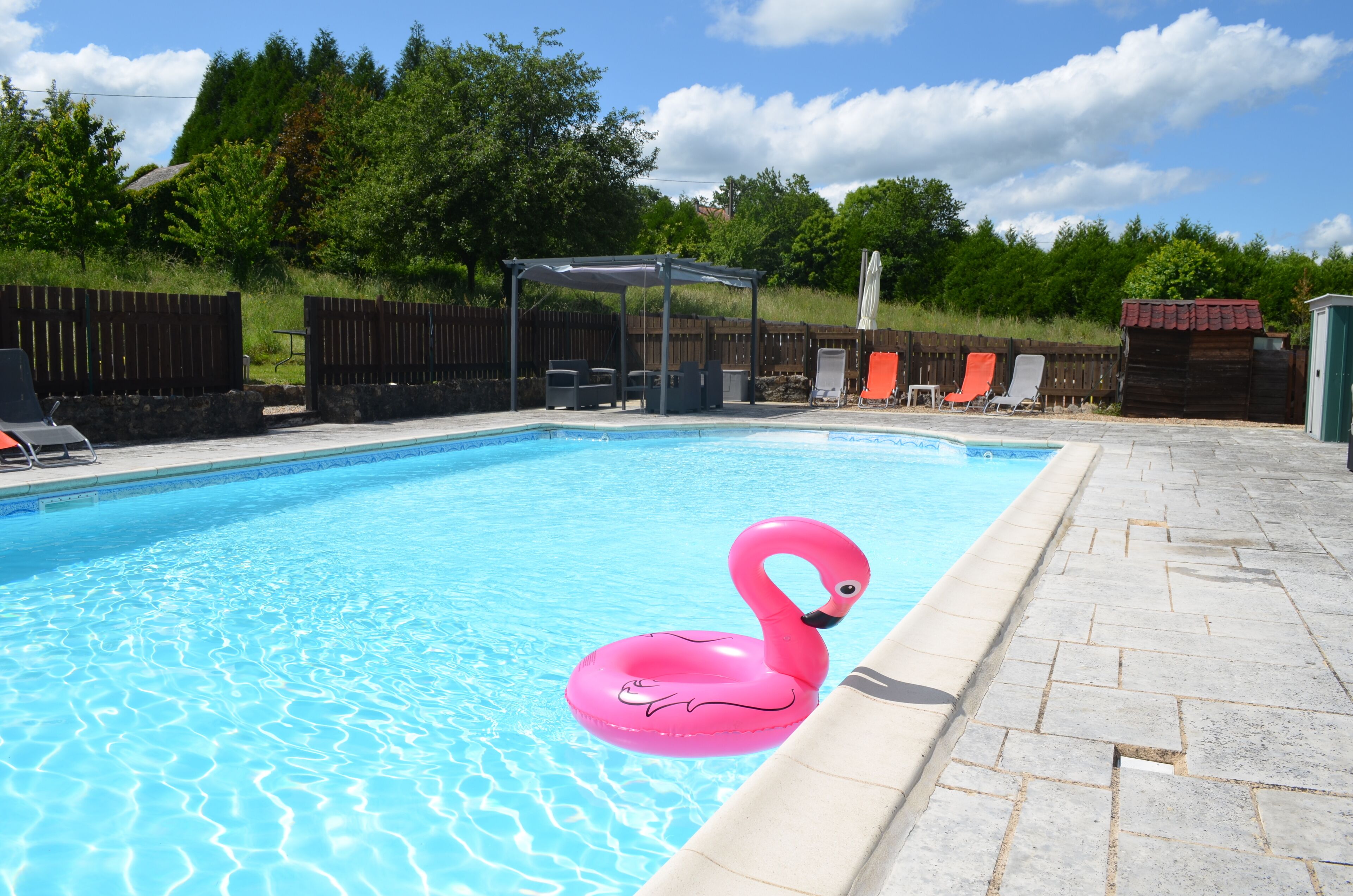 A swimming pool with a pink flamingo float, lounge chairs, and a covered seating area.