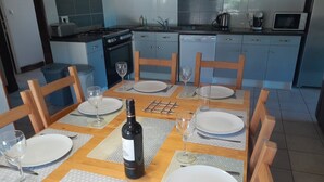 Tavolo da pranzo apparecchiato con piatti, bicchieri da vino e una bottiglia di vino in una cucina moderna con mobili azzurri e piano cottura a gas.