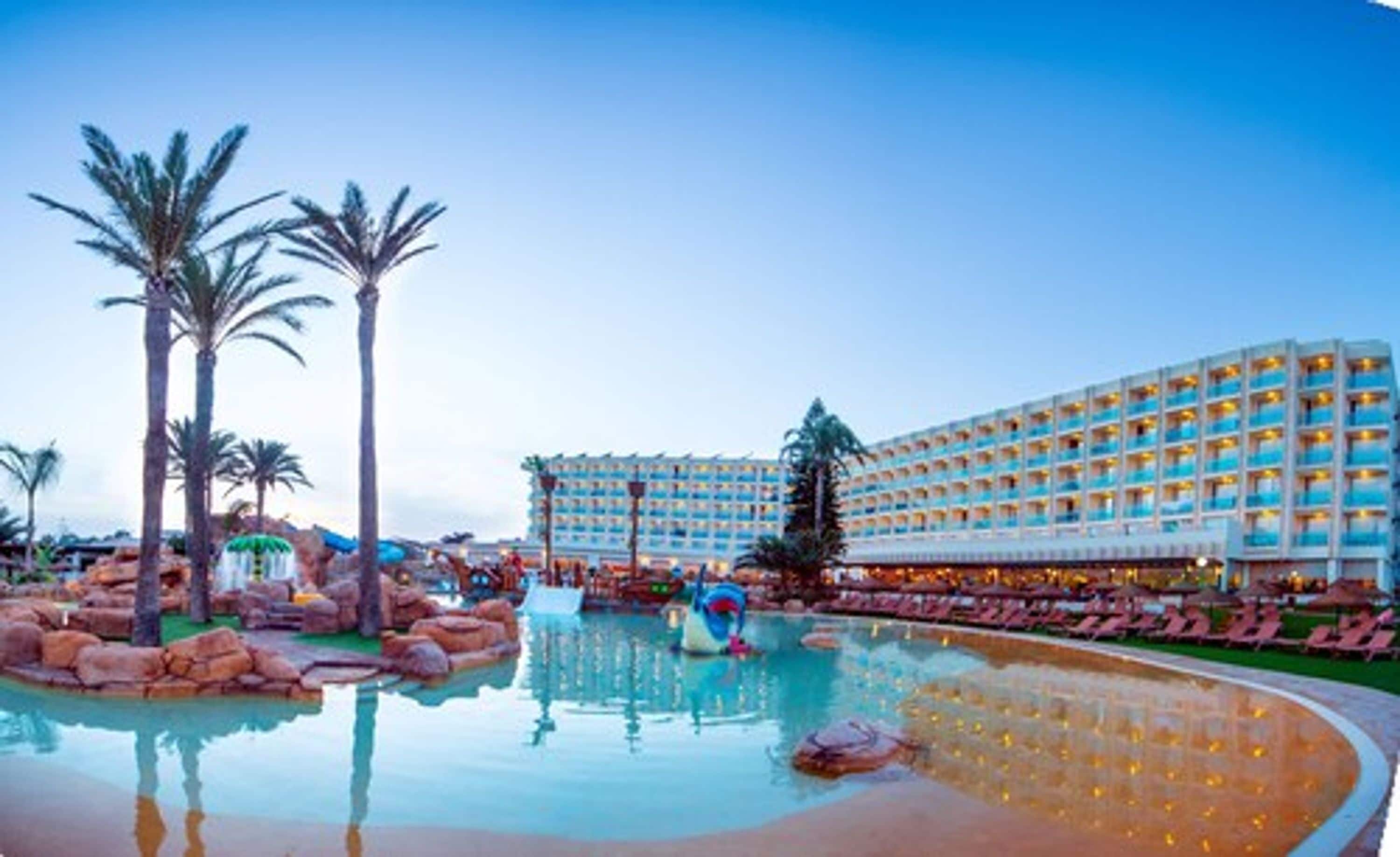 A hotel with a large pool, palm trees, and a water fountain.