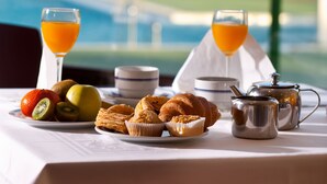 A breakfast table with fruits, pastries, and drinks, overlooking a pool and palm trees. - Evenia Zoraida Resort (Roquetas de Mar)