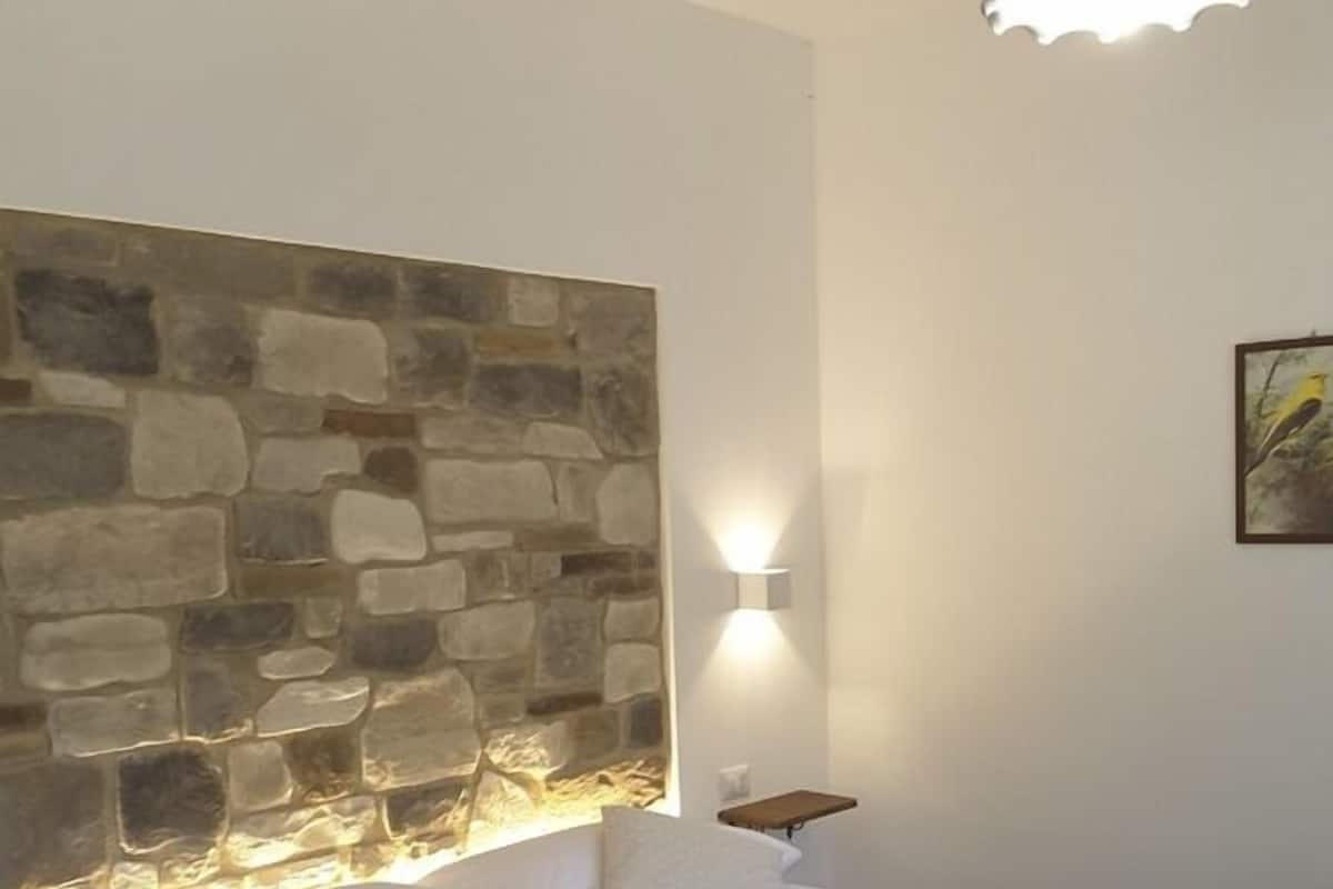 A bedroom with a stone headboard, a bed with white bedding, a nightstand, and a wall-mounted light fixture.