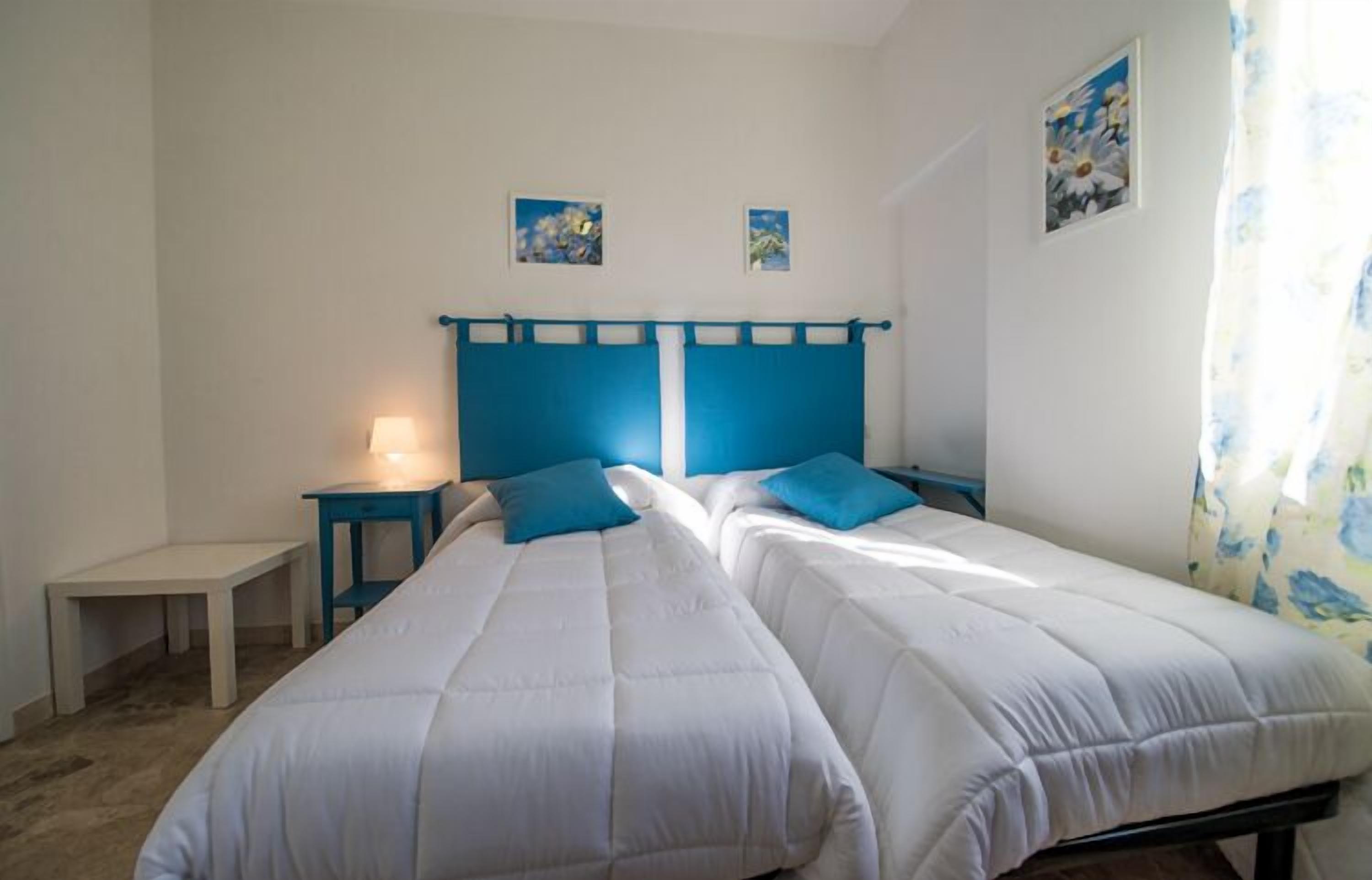 A bedroom with two beds, a nightstand, a lamp, and a small table.