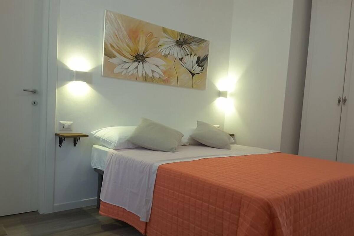 A bedroom with a bed, two bedside tables, a nightstand, a wall-mounted painting, and a wardrobe.