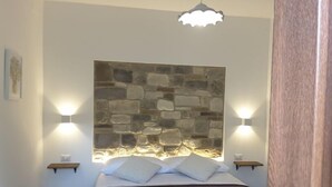 Une chambre avec une tête de lit en pierre, deux lampes de chevet et un luminaire suspendu.