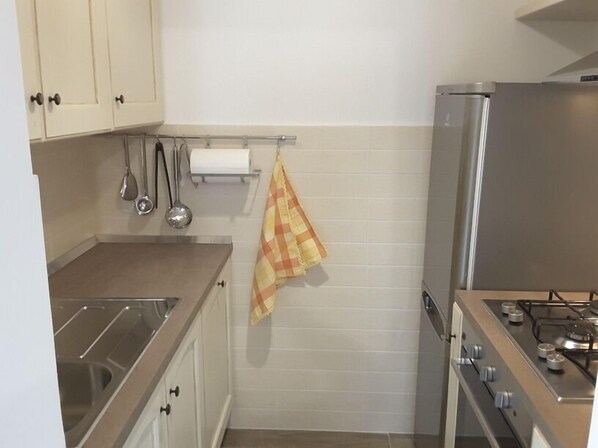 A kitchen with white cabinets, a stainless steel sink, a gas stove, and a hanging yellow checkered towel. - Country House Le Margherite (Montefalcone Appennino)