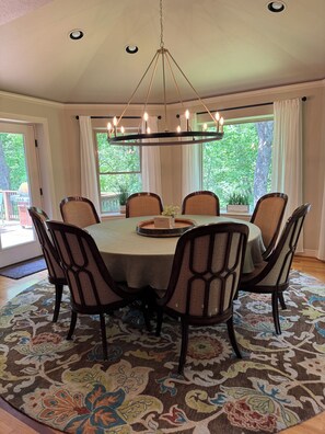 Un coin repas comprenant une table ronde, six chaises, un lustre et de grandes fenêtres avec des rideaux.