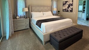 Een slaapkamer met een bed, een plafondventilator, een nachtkastje, een lamp, een dressoir en een schilderij aan de muur.