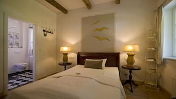 A bedroom with a wooden headboard, two bedside tables with lamps, a bed with white bedding, a wall-mounted shelf with decorative items, and a checkered floor.