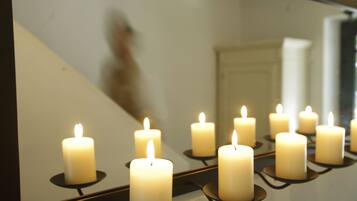 A row of lit candles on a reflective surface, possibly a mirror, with a staircase in the background.
