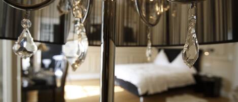 Un candelabro con detalles de cristal, una cama con ropa de cama blanca y un suelo de madera en una habitación con pared a rayas y un espejo.