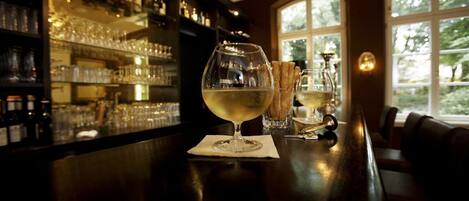A bar area with a wine glass and glasses on the counter, shelves with bottles and glasses, and a window with a view of greenery.