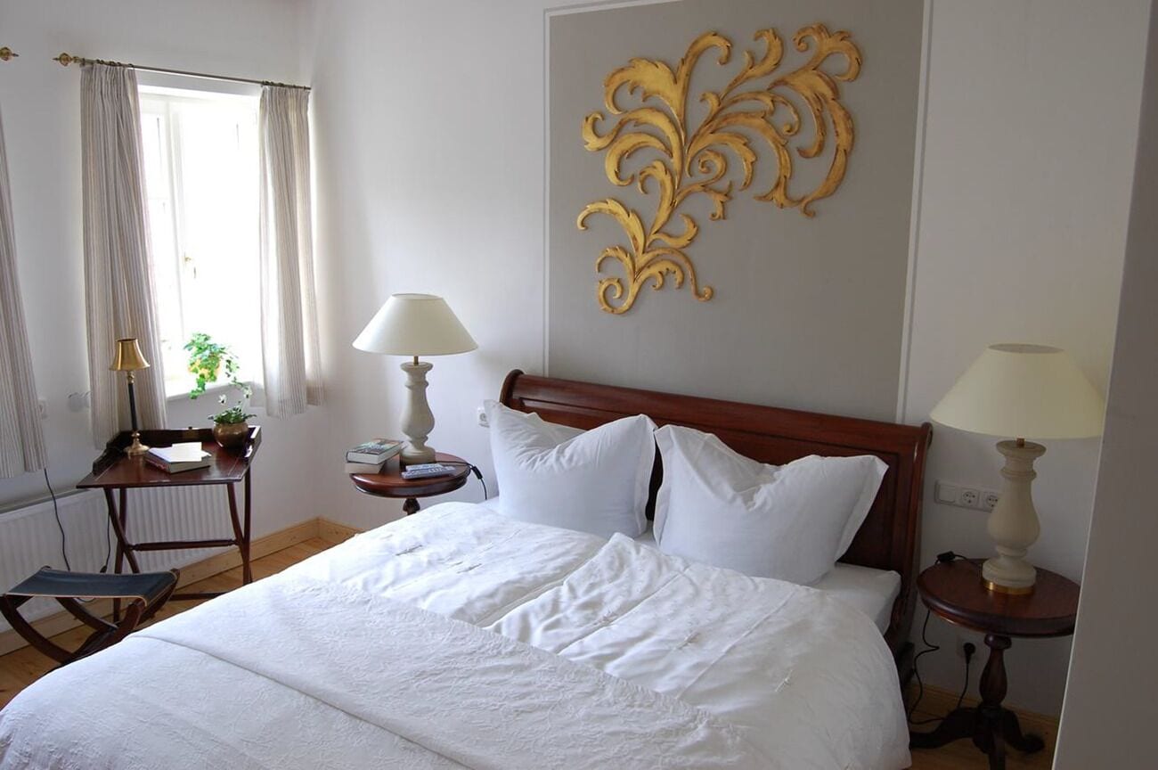 A neatly made bed with white linens, a wooden headboard, and two bedside tables with lamps.