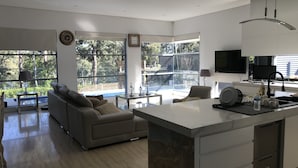 A modern kitchen with a large island, a dining area with a sofa, and a view of a swimming pool. - Luxury big house cinema pool many guests (North Rocks)