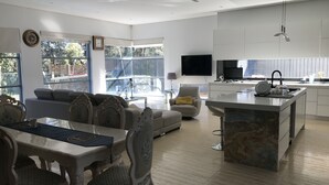A modern living room with a dining area, a kitchen, and a large window. - Luxury big house cinema pool many guests (North Rocks)