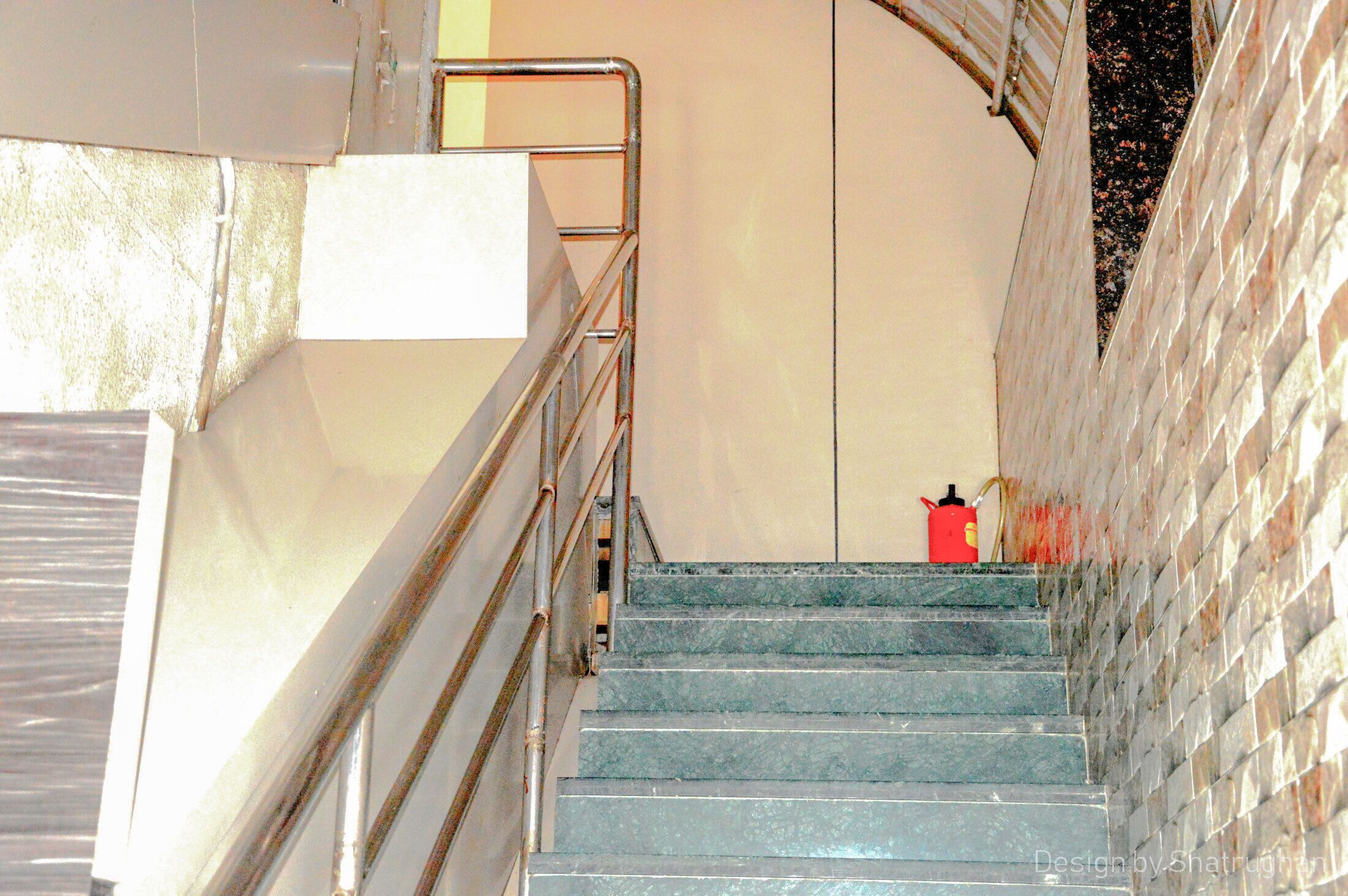 Un escalier avec des rampes en métal, un extincteur et un mur à motifs.