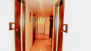 A narrow hallway with wooden doors on either side, leading to a room with a tiled floor. - Hotel Sarovar Grand (Panvel)