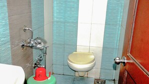 A bathroom with a toilet, a sink, and a red fire extinguisher. - Hotel Sarovar Grand (Panvel)