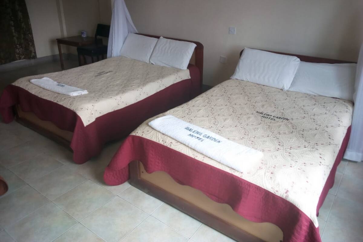 Two twin beds with matching red and beige bedding, a small table, and a chair in a room with plain walls.