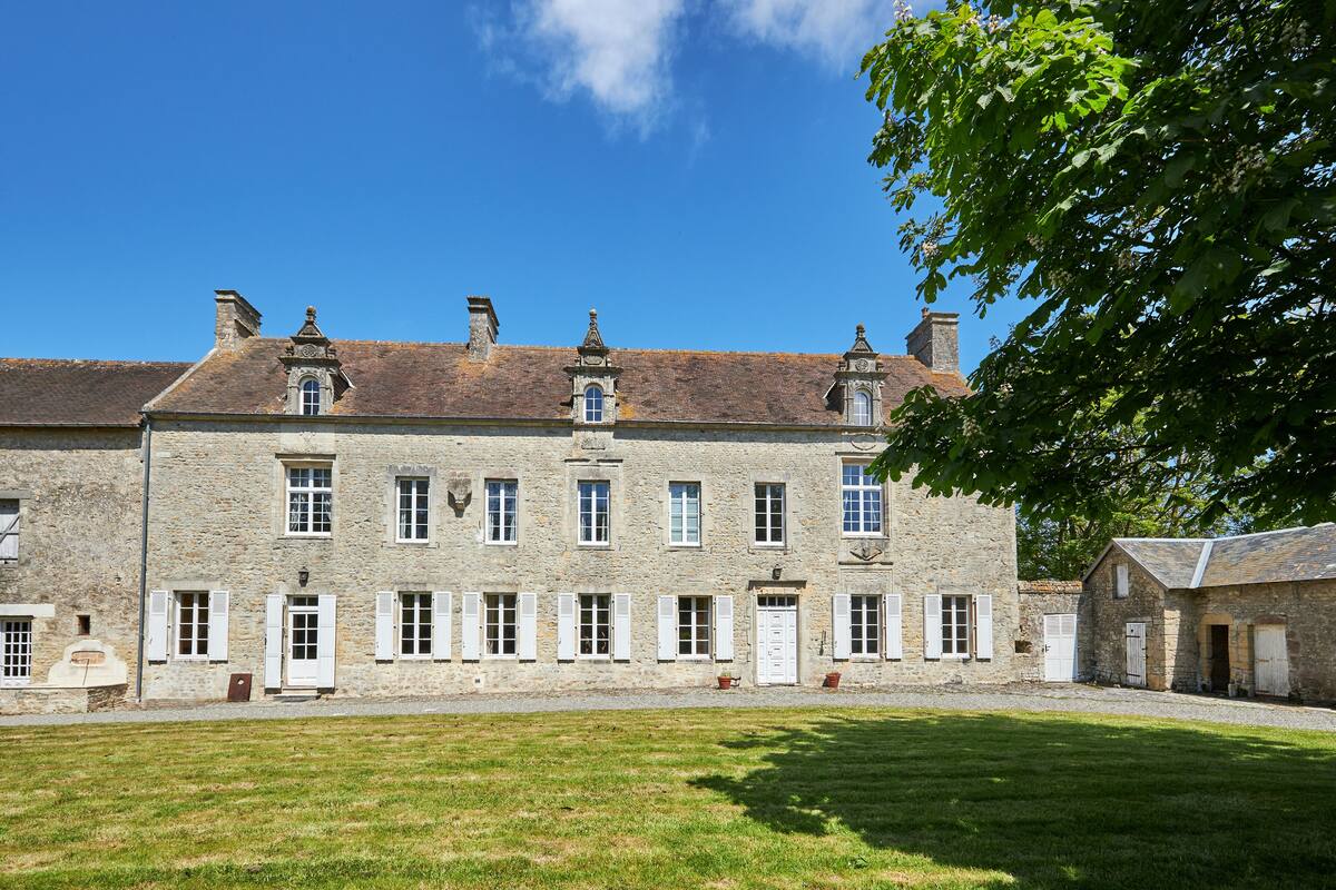 Ein historisches Steinhaus mit zahlreichen Fenstern und Türen, einem Innenhof und einem Baum.