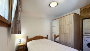 A bedroom with a wooden bed, a nightstand, a mirror, and a washing machine.