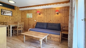 A room with wooden walls, a sofa, a dining table with chairs, and a small table.