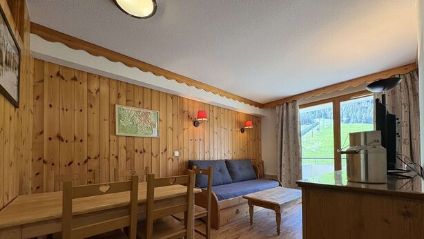 A wooden interior with a dining table, chairs, a sofa, and a small table with a kettle.