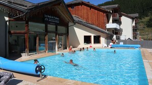 A swimming pool area with a wooden building labeled "Les Hauts de Préalux" and a mountain in the background.