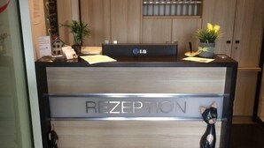A reception desk with a sign reading "RECEPTION" and a welcome mat that says "Herzlich Willkommen Hotel Triton Köln". - Apartmenthaus Triton (Cologne)