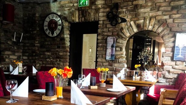 A restaurant with stone walls, wooden tables, and red upholstered chairs. - Apartmenthaus Triton (Cologne)
