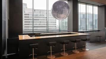 A modern bar area with a large window, a hanging spherical light fixture, and a bar counter with stools.