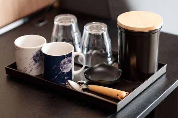 Una bandeja con dos tazas, un termo, una cuchara y una espátula sobre una superficie de madera oscura.