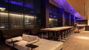 Een moderne bar met een lange toonbank, barkrukken en een bank.