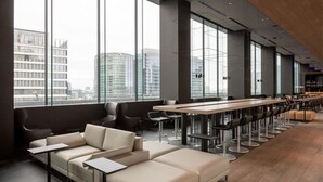 Een moderne lounge met een lange tafel en meerdere stoelen, grote ramen met uitzicht op de stad, en een zithoek met banken en tafels.