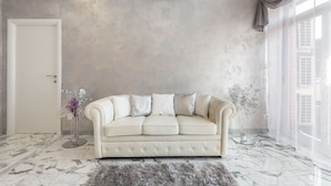 A modern living room with a cream-colored sofa, marble flooring, and a large window with curtains. - Luxury Rome Guest House (Rome)
