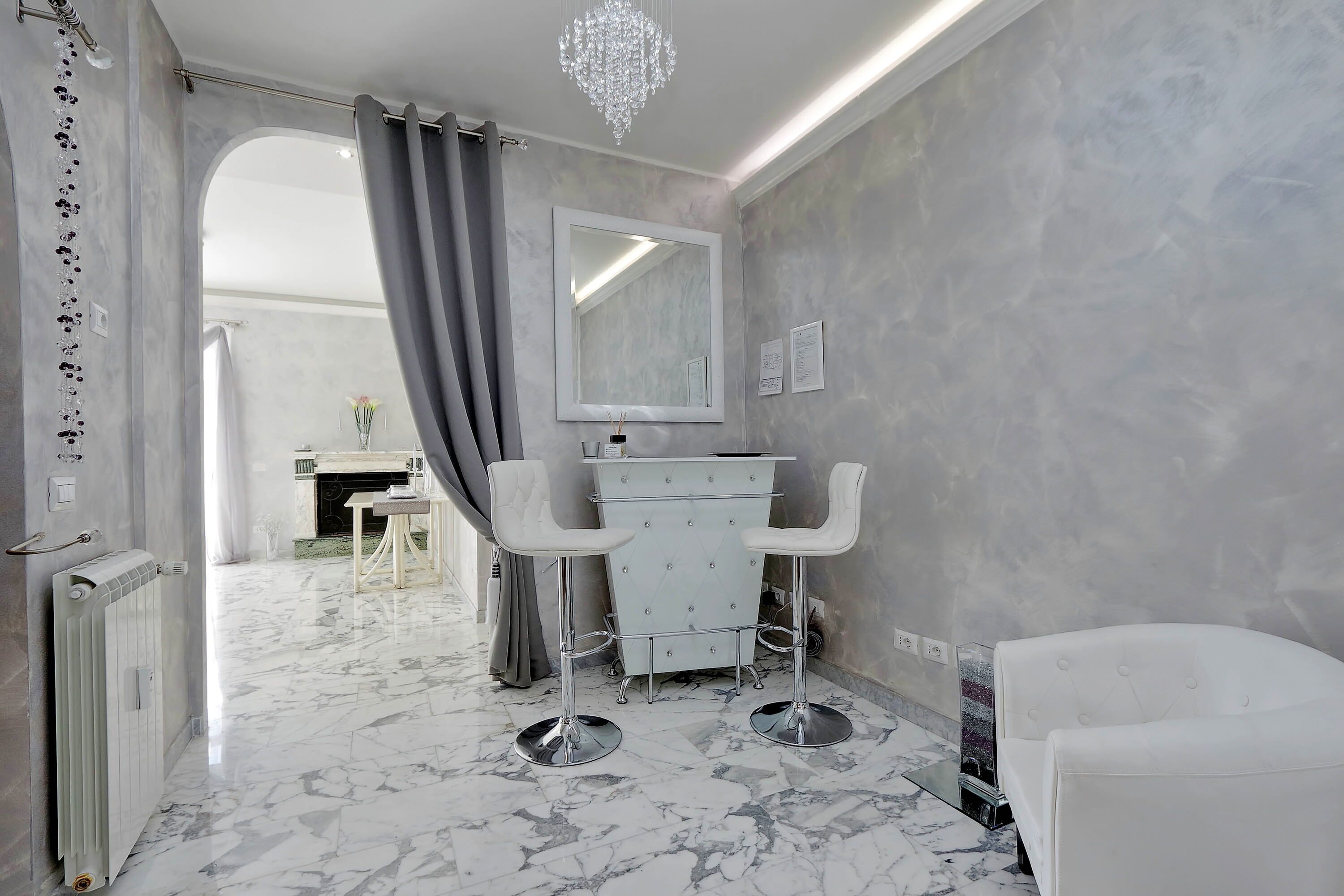 A modern bathroom with a marble floor, a white vanity, two bar stools, and a large mirror.