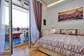 A bedroom with a large bed, a painting of a cityscape, and a view through a glass door to an outdoor area with a table and chairs. - Luxury Rome Guest House (Rome)