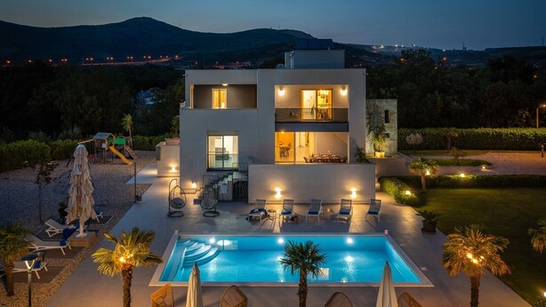 Un bâtiment moderne à deux étages, doté d’une piscine, d’un espace extérieur aménagé et offrant une vue sur les montagnes.