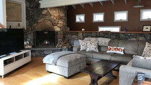 A living room with a stone fireplace, a grey sectional sofa, a flat-screen TV, and a wooden coffee table.