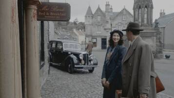 Un coche antiguo estacionado frente a un edificio con un letrero que dice 'Mrs. Brown's Bed & Breakfast'.