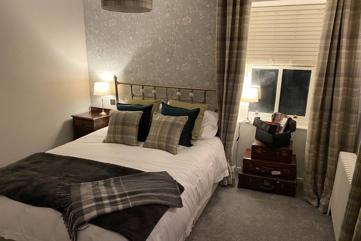 A neatly made bed with a plaid throw blanket, a headboard with decorative elements, and a nightstand with a lamp.